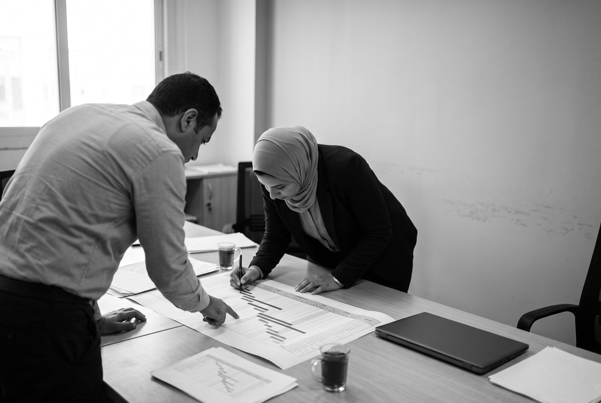 Two colleagues working over a printed project schedule in a Cairo office